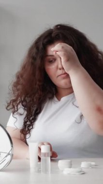 Dikey video. Göz bakımı altında. Deri rutini. Kozmetik ürünü. Yaşlanma karşıtı tedavi. Kilolu obez kadın temiz yüzüne nemlendirici krem sürüyor..