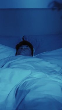Dikey video. Kötü bir rüya. Gece dehşeti. Uyku korkusu. Korkmuş bir adam, karanlık yatak odasındaki şeytani el gölgesi kâbusundan uyandı..
