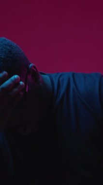 Dikey video. Hayal kırıklığı hatası. Hata sorunu. Hayal kırıklığına uğramış adam, burgonya arka planında izole edilmiş neon ışıkla yüzünü kapatan sorunlu ellerle vurguladı..