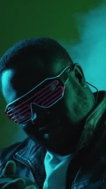 Dikey video. Siber punk partisi. Neon dansı. Gece hayatı eğlencesi. Havalı stil sahibi, modaya uygun, fütürist gözlüklü, renkli, parlak dumanlı gece kulübü müziğinin tadını çıkaran adam..
