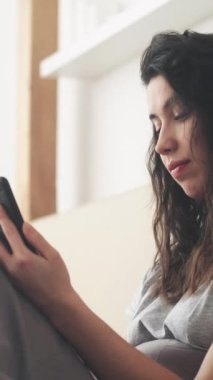 Dikey video. Telefon tartışması. Mobil çatışma. Siber zorbalık. Hayal kırıklığına uğramış bir kadın aydınlık yatak odasında akıllı telefondan mesaj atıyor..