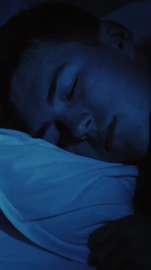 Dikey video. Kabus korkusu. Uyku bozukluğu. Korkmuş korkmuş adam uyandı. Gece geç saatte koyu mavi ışıkta gözlerini açtı..