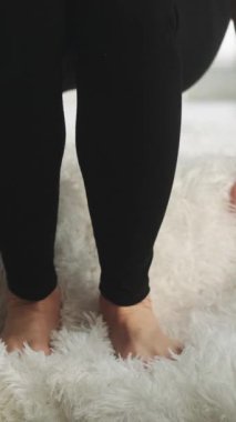 Dikey video. Düz taban. Bacakları ağrıyor. Ayak masajı. Yorgun tabanları ovuşturan kadın yumuşak yumuşak beyaz halıda rahatsız ayakkabılar yüzünden acı çekiyor..