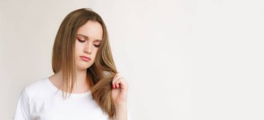 Saç terapisi. Onarım tedavisi. Beyaz tişörtlü, hayal kırıklığına uğramış güzel bayan arka planda izole edilmiş hasarlı kötü sonlara bakıyor..