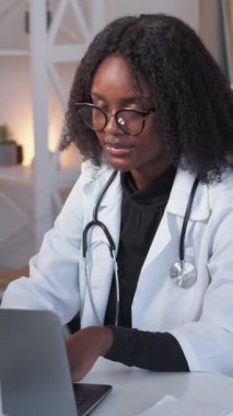 Dikey video. Dijital sağlık hizmeti. Klinik servisi. Güvenilir güler yüzlü kadın doktor. Hastane çalışma masasında laptopta çalışan pratisyen hekim..