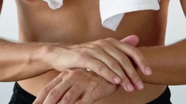 El bakımı. Cilt nemlendirici. Tanınmayan atletik bir adam havluyla tüp içinden krem sürüyor avuç içlerine sürtünüyor ve beyaz arka planda izole edilmiş parmakları var..