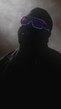 Dikey video. Rap tarzı. Gece kulübü sanatçısı. Moda gözlüklü modern hip hop sanatçısı karanlık sahne arkasında dumanlı bir partide şarkı söylüyor..