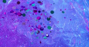 Parlak sıvı. Konfeti döküldü. Dekoratif kıvılcımları olan su mor buz yüzeyinden aşağı akar. Bulanık mürekkep neon efektli renkli arkaplan.