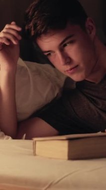 Dikey video. Gece kitabı. Yorgun genç bir adam huzurlu bir ortamda uykuya dalıyor. Derin düşüncelere dalmış huzurlu bir ışıkla banyo yapıyor..