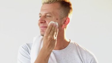 Yüz temizleme. Cilt bakımı. Sivilce tedavisi. Beyaz fotokopi arkaplanında izole edilmiş pamuk pedi kullanarak kendine güvenen sarışın adam tonikle yüzünü temizliyor..