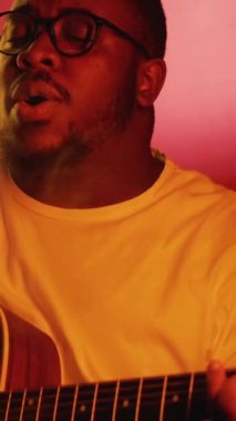 Dikey video. Vokalist gösterisi. Akustik festivali. Yetenekli müzisyen gitarist telli enstrüman çalıyor. Parlak neon ışığı altında duman içinde şarkı söylüyor..