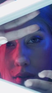 Dikey video. Neon ışıklı surat. Siber punk güzeli. Estetik kozmetoloji. Pembe mavi renkli, dumanlı şehvetli bir kadın. Karanlık arka planda beyaz LED lamba ışığıyla poz veriyor..