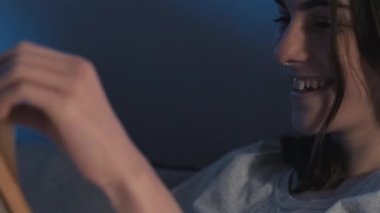 Gece okumaları. Yatak hobisi. Neşeli, meraklı kız kitap eğlenceli hikayesiyle eğleniyor. Gece geç saatlerde ev odasının karanlığında gülüyor..