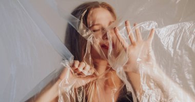 Acı çeken bir kadın. Derin nefes al. Üzgün depresif kadın kırışık şeffaf polietilen filmin arkasına sıkışmış. Gri üzerine izole edilmiş..