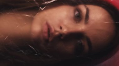 Dikey video. Kadın koruması. Etkisiz hale getirilmiş portre. Sosyal izolasyon. Kırmızı turuncu parlaklıktaki buruşuk dokuya bakan yorgun kadın..