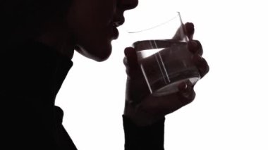 Su dengesi. Sıvı diyeti. Tazeleme detoksu. Koyu renk kontrast profilli siluet, beyaz boşlukta izole edilmiş bardaktan saf mineral içen susamış kadın silueti..