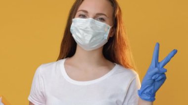 Karantina eğitimi. Okul yeniden açılıyor. Koruyucu maske eldivenli neşeli bayan öğrenci sarı fotokopi arkaplanında izole edilmiş zafer hareketi gösteriyor..