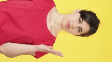 Dikey video. Kararsız kadın. Şüphe uyandırıyor. Kafa karışıklığı, şüpheci dargınlık, sarı serbest alan arka planında izole edilmiş..