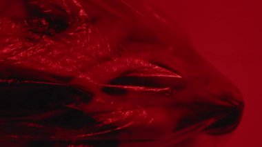 Dikey video. Nefes darlığı. Solunum bozukluğu. Acı çeken kadın, saydam polietilen filmde sıkışıp kalmış. Odaktan çıkmış koyu kırmızı renkte izole edilmiş..