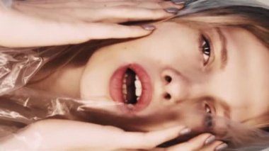 Dikey video. Anksiyete krizi. Zihinsel bozukluk. Polietilen film kapüşonlu rahatsız güzel bir kadının bej rengi üzerinde baygınlık geçiren bir sanat portresi..