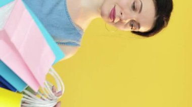 Dikey video. Alışveriş fiyaskosu. Üzgün müşteri. Alışverişkolik kadın, sarı boş alan arka planında izole edilmiş başka bir alıcıya kese kâğıtlarını kaybetmekten bıktı..