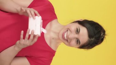 Dikey video. Beklenmedik bir hediye. Kadın hediye alıyor. Rüya tatmini. Mutlu bir mutluluk. Sarı arka planda izole edilmiş bir kutu..