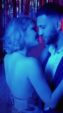 Dikey video. Romantik dans. Parti çifti. Gece randevusu. İlişki yıldönümü. Sevgi dolu bir kadın, koyu mavi ışıklı erkek arkadaşıyla kutlama yapıyor..