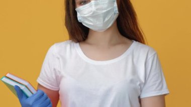 Karantina eğitimi. Sosyal uzaklık. COVID-19 salgın enfeksiyonu önleme koruyucu maske eldivenli kadın öğretmeni rahatlattı ve sarı fotokopi alanında izole kitaplar bıraktı..