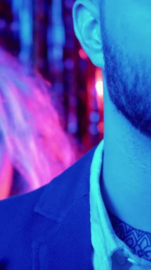 Dikey video. Romantik parti. Neon ışıklı çift. Tatil bağı. Sevgi dolu bir kadın, mavi pembeli erkek arkadaşını kucaklıyor. Parlak parlak süslemelerde parlıyor..