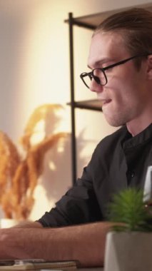 Dikey video. Fikir geliştirme. Çevrimiçi terfi. Gözlüklü, siyah, modern tişörtlü, dizüstü bilgisayarında yazan yaratıcı adam..