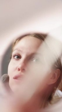 Dikey video. Kız makyajı. Güzellik kozmetiği. Çekici genç bayan elinde pudra fırçasıyla hazırlanıyor. Aynadan yansımaya bakıyor..