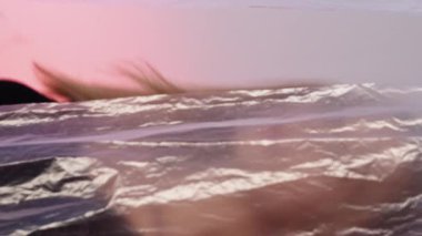 Dikey video. Kadın koruması. Kız portresi. Şehvetli, kendine güveni olmayan bir kadın pembe mavi renk eğimli polietilen film üzerinde kırışık dokunun arkasında yürüyor..