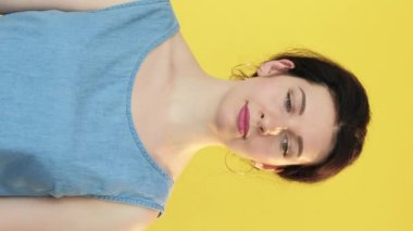 Dikey video. Alışveriş yarışması. İndirimli satış. Başka bir müşteri tarafından taşınan renkli kağıt torbalara bakan şaşkın kadın sarı boş alanda izole edilmiş..