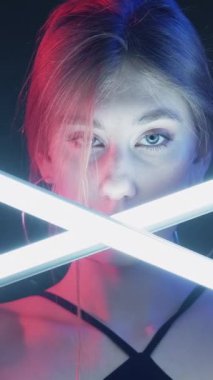 Dikey video. Neon ışıklı kız. Fütürist moda. Disko gece hayatı. Pembe mavi, parıldayan kadın, yüzü koyu renkli, beyaz, LED lamba ışığına bakıyor..