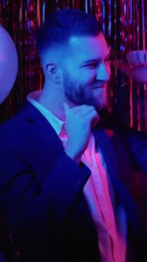 Dikey video. Parti insanları. Yeni yıl kutlaması. Şen şakrak. Mutlu, rahat, mutlu, gülümseyen çift mavi, neon ışıklı dumanda dans ediyor..