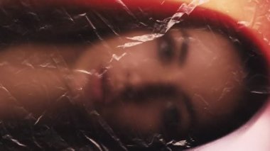 Dikey video. Kadın özgürlüğü için. Güzellik kızı. Kırışık dokuda solgunlaşan rahatsız bir kadın. Kırmızı turuncu parıltılı polietilen film odak dışı..