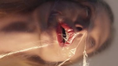 Dikey video. Nefes darlığı. Astım hastası. Kırışık şeffaf plastik polietilen filmin arkasında sıkışmış ızdırap çeken bir kadın..