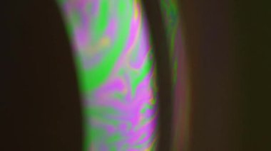 Dikey video. Renk karışımı. Psikedelik boya. Pembe, parlak, yeşil yağ kabarcığı sıvısı koyu siyah soyut sanat arka planında holografik eğri içinde harmanlanır..