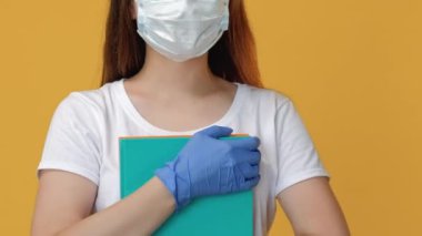 Salgın öğretmen. Karantina eğitimi. Sosyal uzaklık. Korunaklı yüz maskesi eldivenli, sarı kopya boşluğunda izole edilmiş kitapları olan kendine güvenen bir bayan öğrenci..