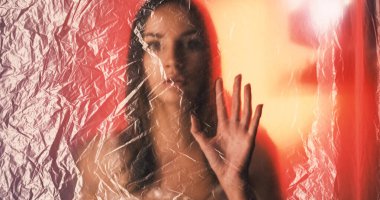 Kadın özgürlüğü için. Güzellik kızı. Odaklanamayan rahatsız kadın, kırmızı turuncu parlaklıktaki buruşuk desenli polietilen filmle odak arkaplanından kayboluyor..