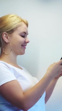 Dikey video. Çevrimiçi mesaj. Akıllı telefon sohbeti. Mutlu, mutlu, gülümseyen bir kadın beyaz renkli boş arkaplanda modern cihaza mesaj yazıyor..