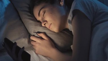 Mobil uykusuzluk. Uykusuzluk. Yorgun, uykulu bir kadın gecenin geç saatlerinde karanlık bir yatak odasında telefonla uyuyakalıyor..