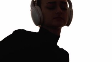 Dans eden siluet. Müzik zevki. Kulaklıklı heyecanlı kadının, beyaz boş alanda izole edilmiş ses aygıtını dinlemenin keyfini çıkardığı koyu renk kontrast çizgisi..