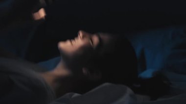 Romantik sohbet. Gece online. Randevu uygulaması. Rahatlamış mutlu aşık bir kadın telefonda gülümseyen bir mesaj okuyor geç saatte yatakta, karanlık odada..