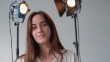 Model pozu. Kadın portresi. Açık renk elbiseli esmer sanatçı kameranın önünde hareket ediyor. Fotoğraf stüdyosundaki kız profesyonel spot ışıkları.