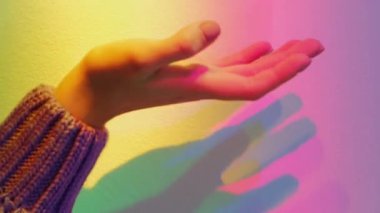 Dikey video. El feneri. Gökkuşağını yakalıyorum. Silah büyüsü. Şehvetli kadın parmakları, arka plandaki renksiz pastel renge dokunuyor..