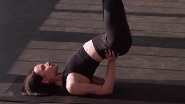 Vücut eğitimi. Fiziksel antrenman. Aktif giyinen atletik kadın, spor salonundaki spor salonundaki yoga minderinin üzerine yatarak omuz duruşu yapıyor..