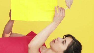 Dikey video. Neşelen biraz. Beklenmedik bir hediye. Şimdiki rüyayı gerçekleştiren kadın mutlu bir şekilde sarı boş alanda izole edilmiş alışveriş torbaları ile mutlu bir şekilde yaşıyor..