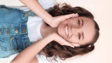 Dikey video. Şaşırtıcı kadın portresi. Haberler iyi. Pozitif duygu, iki at kuyruklu mutlu genci heyecanlandırdı. El çırpıyor, beyaz arka planda sırıtarak gülümsüyordu..