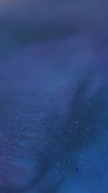 Dikey video. Işıl ışıl. Parıltı hareketi. Odaklanmamış mavi boya parlak mor parçacıklar doku renk karışımı akış soyut sanat arkaplanı.